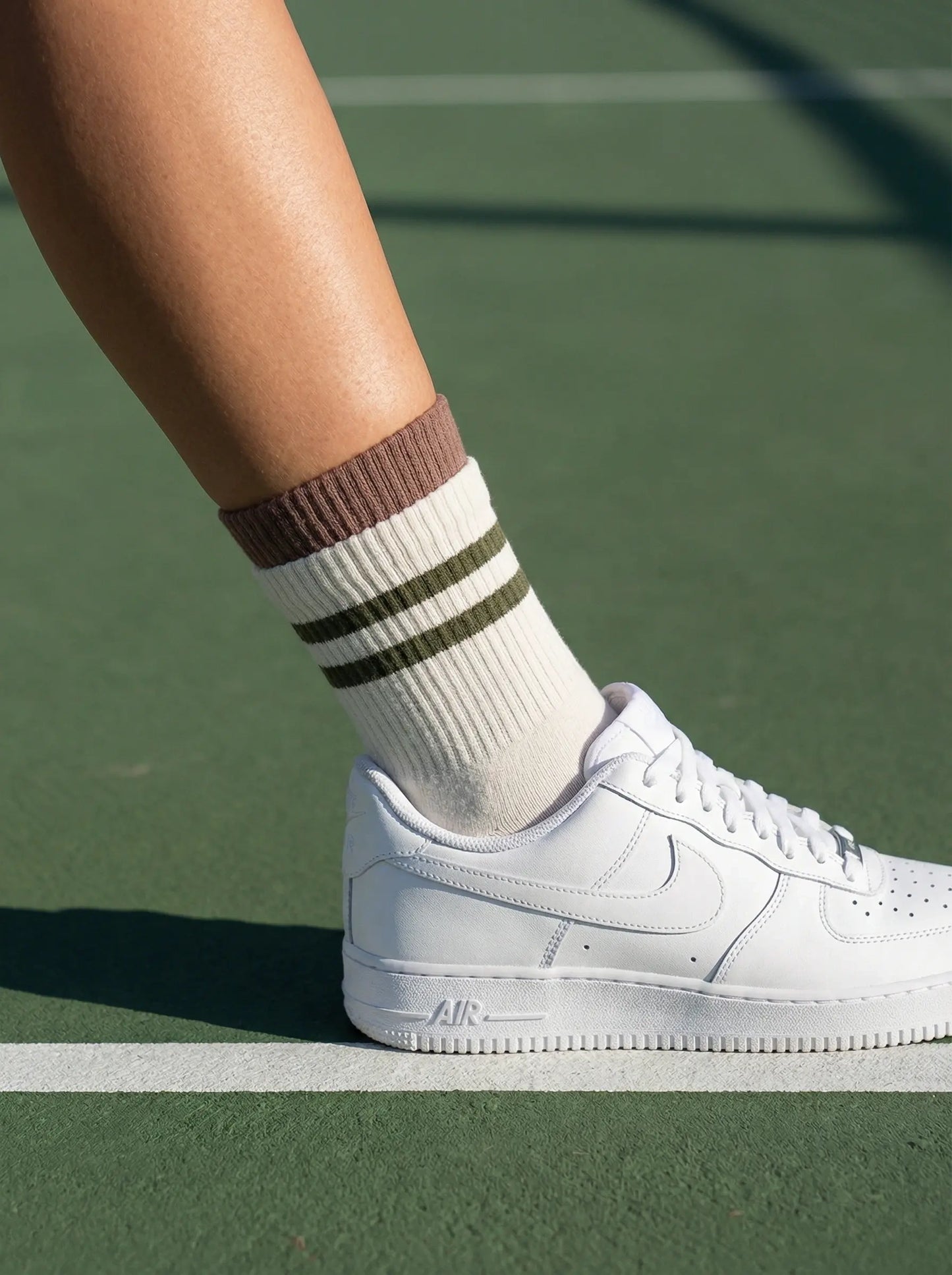 Closeup of layered cuff striped retro grip sock in white colour with green stripe with white sneakers at tennis court side view