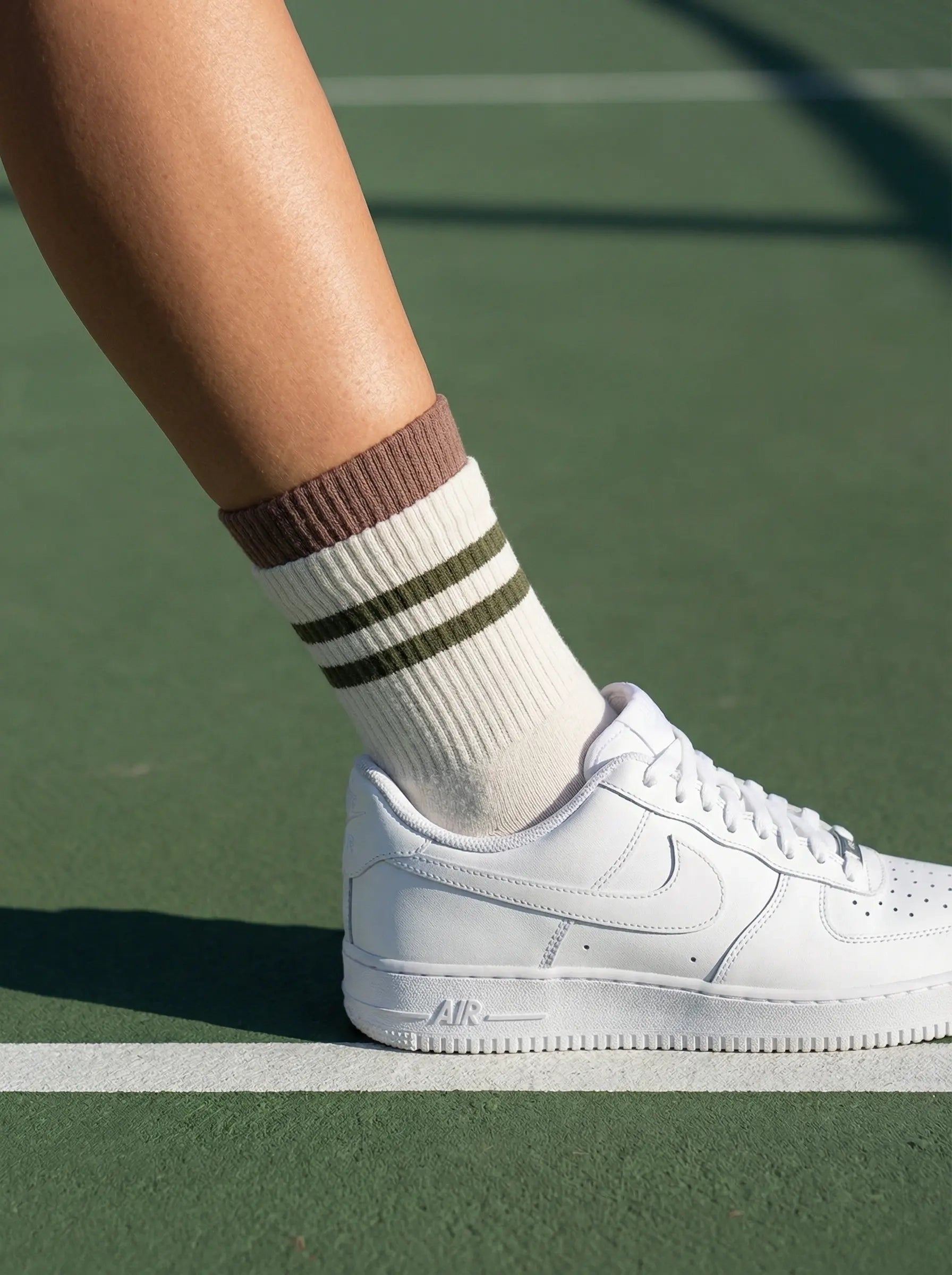 Closeup of layered cuff striped retro grip sock in white colour with green stripe with white sneakers at tennis court side view