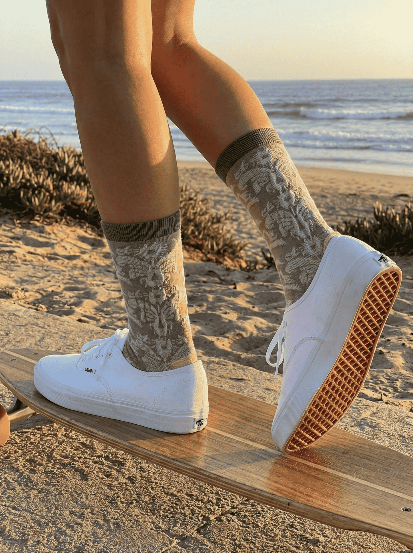 Close-up of taupe jacquard crew sock side view with white sneakers on skateboard at the beach