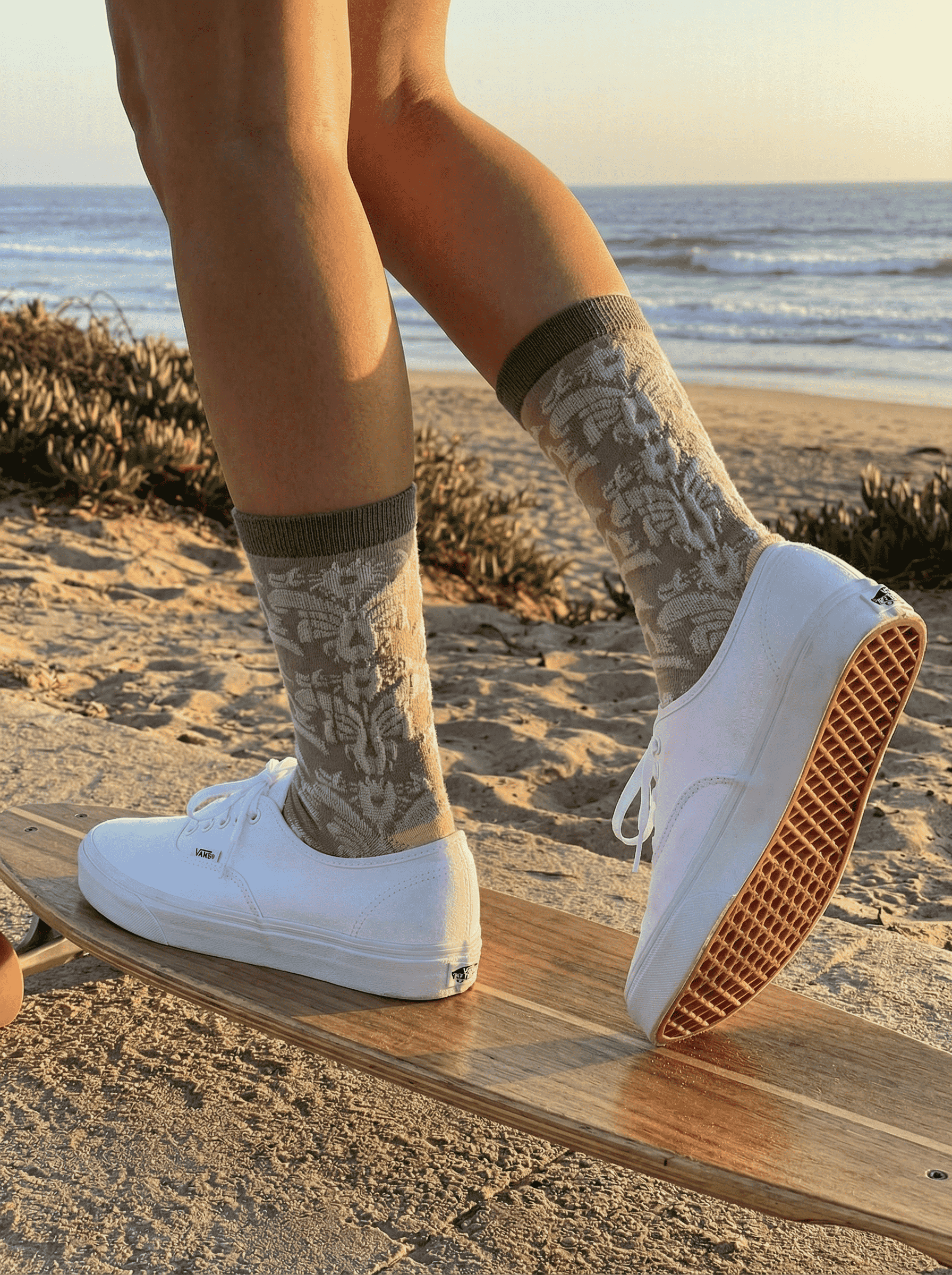 Close-up of taupe jacquard crew sock side view with white sneakers on skateboard at the beach