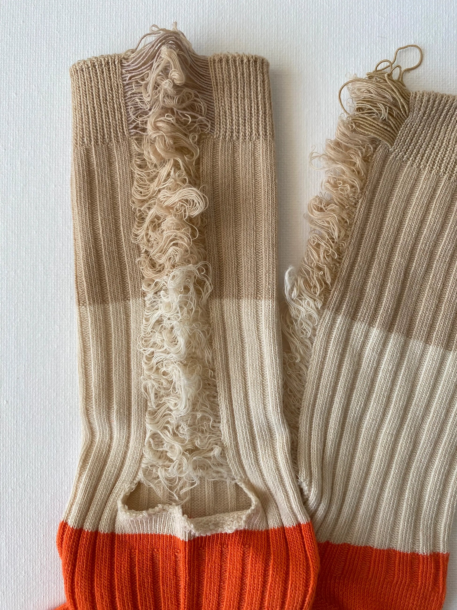 Closeup of the ripped details of unisex crew sock in cream and orange colour 